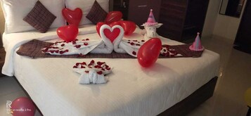Una cama bien hecha con adornos con forma de corazón, una pequeña figurita blanca y un gorro de fiesta rosa.