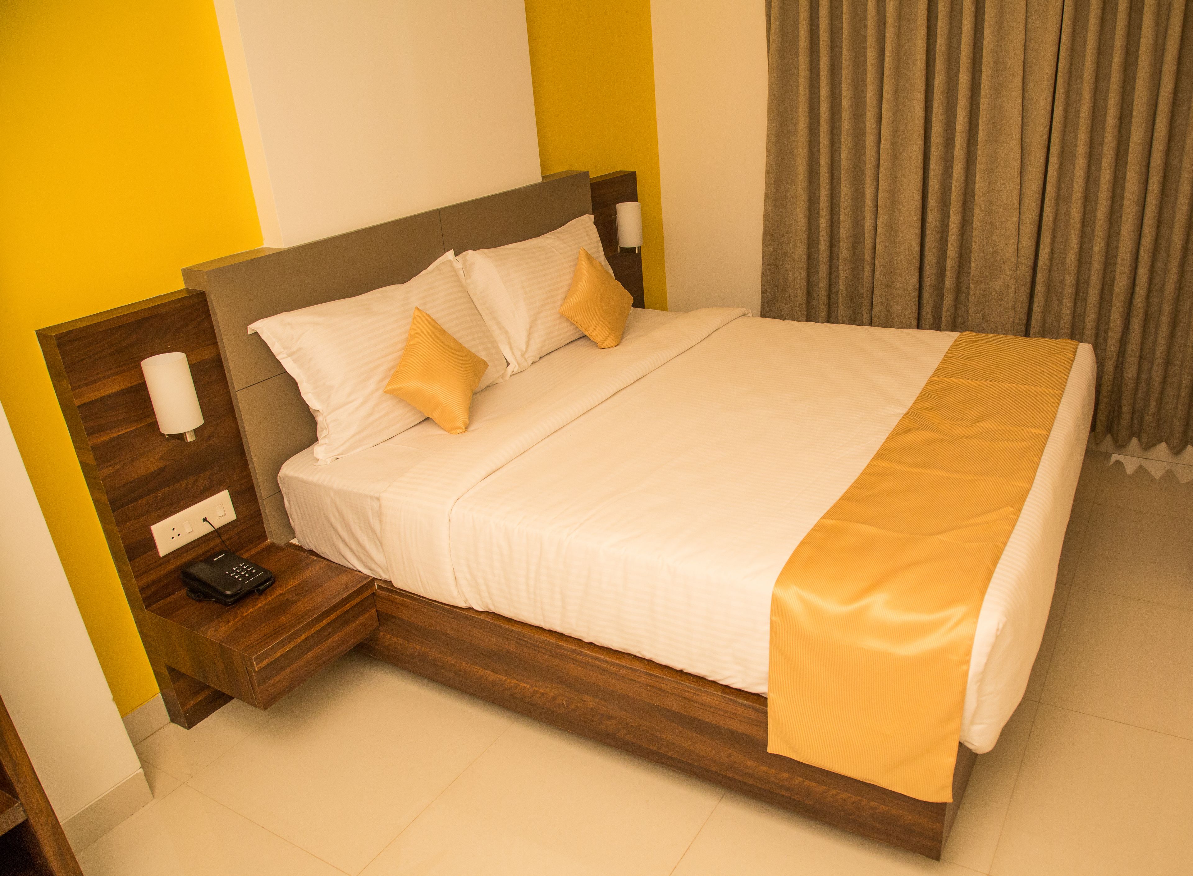 A neatly made bed with a wooden headboard, a bedside table with a lamp, and a power outlet.