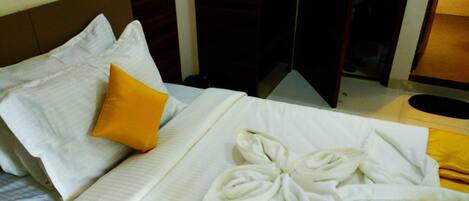 A neatly made bed with white linens and a single yellow pillow, a wooden headboard, and a dark wooden wardrobe.