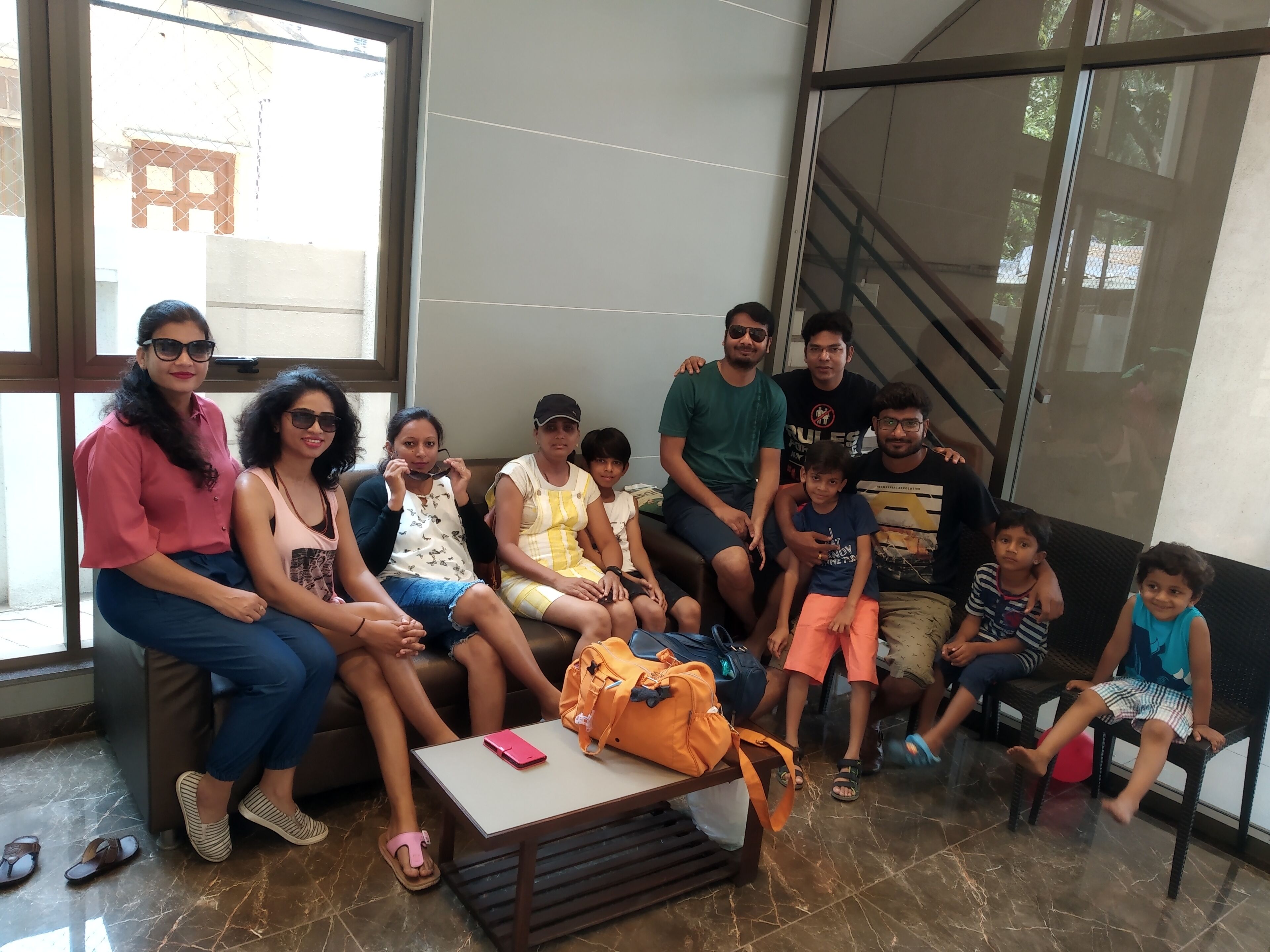 Un grupo de personas sentadas en un sofá y sillas en una habitación con piso de baldosas y una ventana.