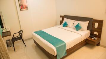 Una cama bien hecha con un plaid verde azulado, un cabecero de madera y dos mesitas de noche con un teléfono y una lámpara.