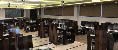 A restaurant with multiple dining tables and booths, each with a dark wood finish and cushioned seating.