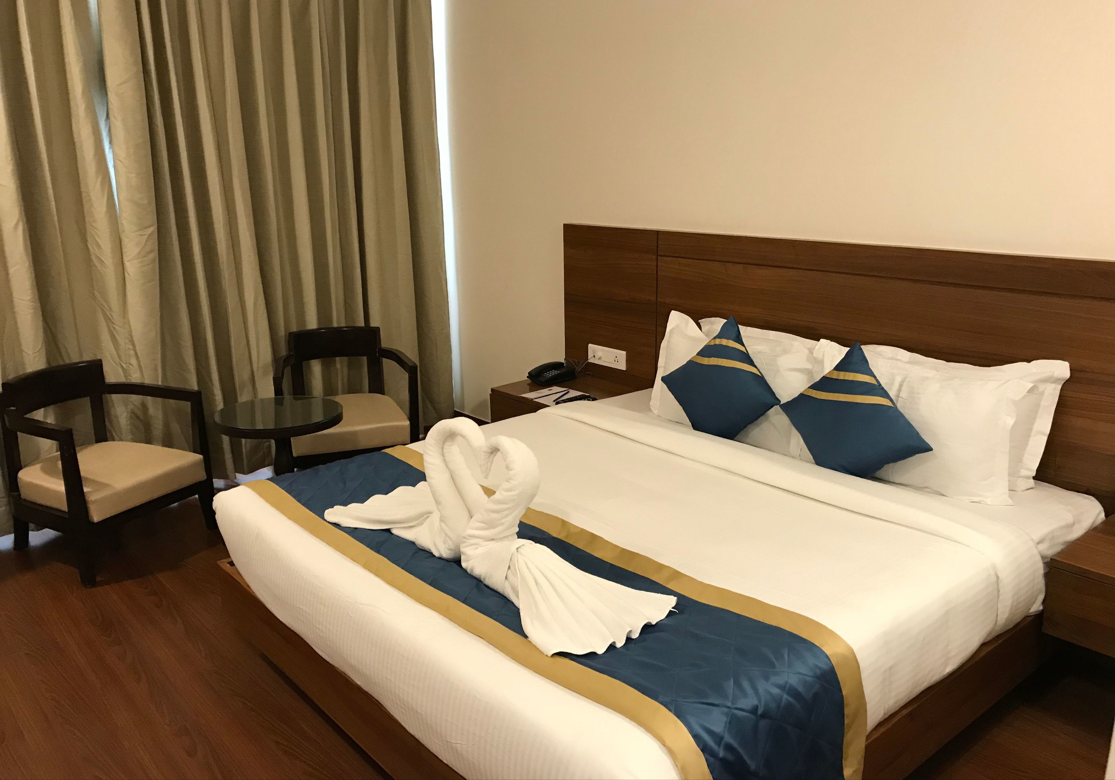 A hotel room with a neatly made bed, a wooden headboard, a small round table with a chair, and a nightstand with a phone.
