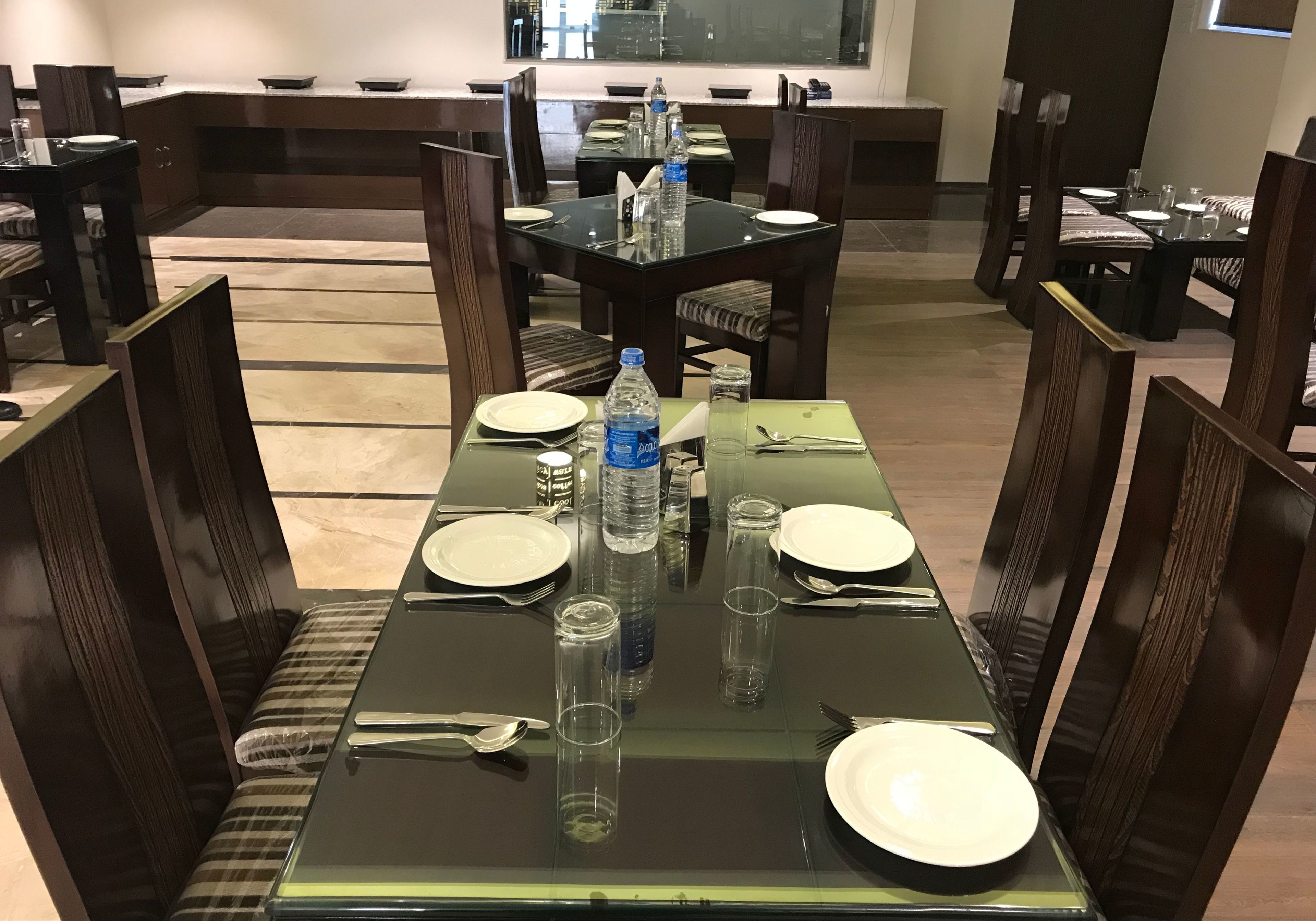 A dining area with tables set for four, equipped with plates, cutlery, and water bottles.