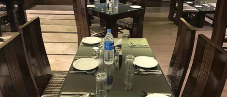 A dining area with tables set for four, equipped with plates, cutlery, and water bottles.