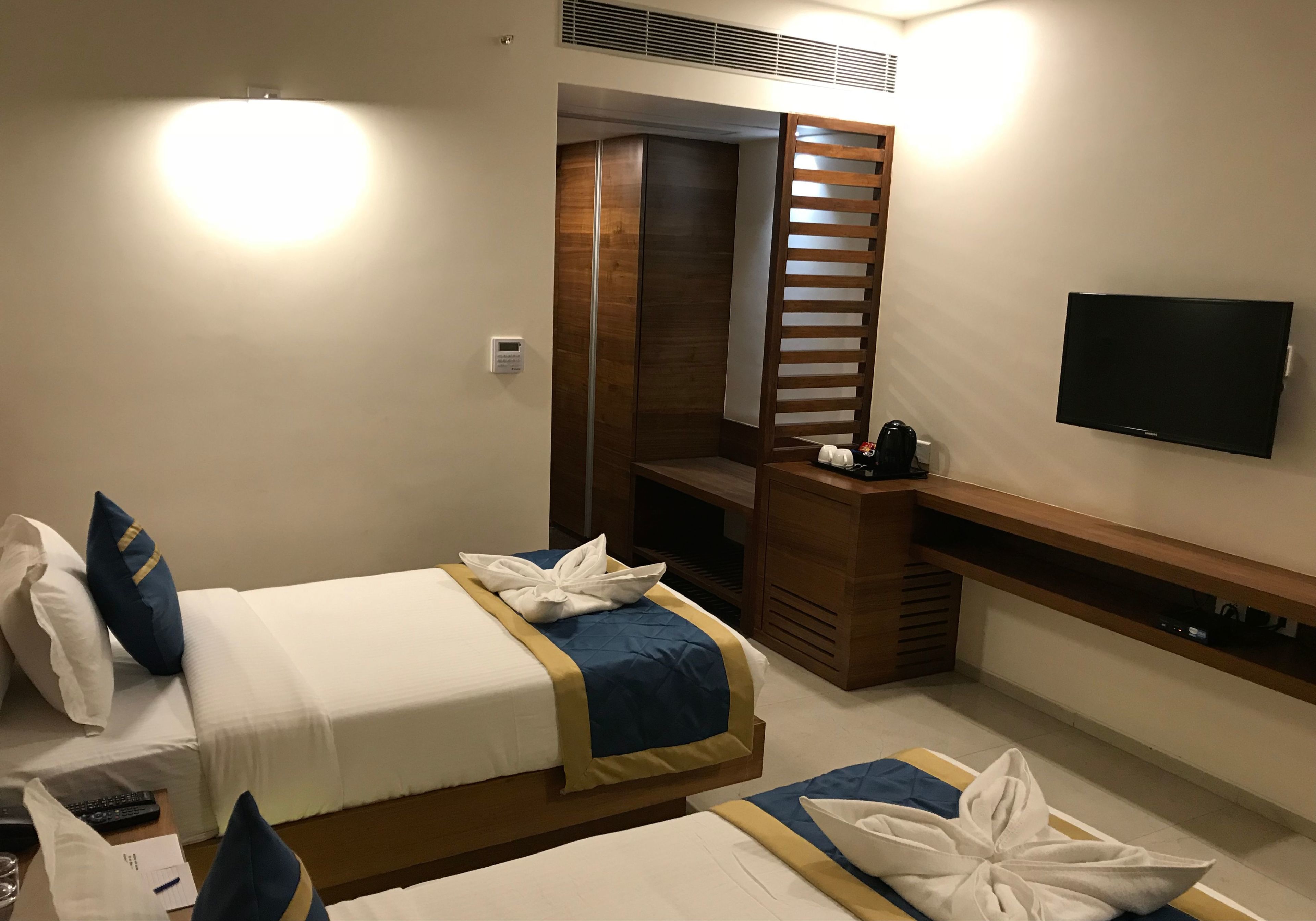 A hotel room with two beds, a TV, a desk, and a wooden partition.