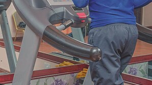 A man using a treadmill in a room with a glass wall and a floral-patterned floor. - Sunshine Hotel (Kericho)