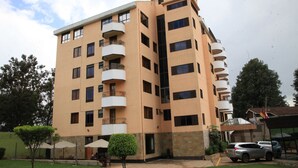 A multi-story building with balconies, a parking area, and a small garden with trees and umbrellas. - Sunshine Hotel (Kericho)