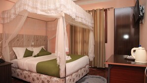 A bedroom with a four-poster bed, a desk, a chair, and a television. - Sunshine Hotel (Kericho)