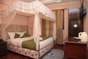 A bedroom with a four-poster bed, a desk, a chair, and a television.