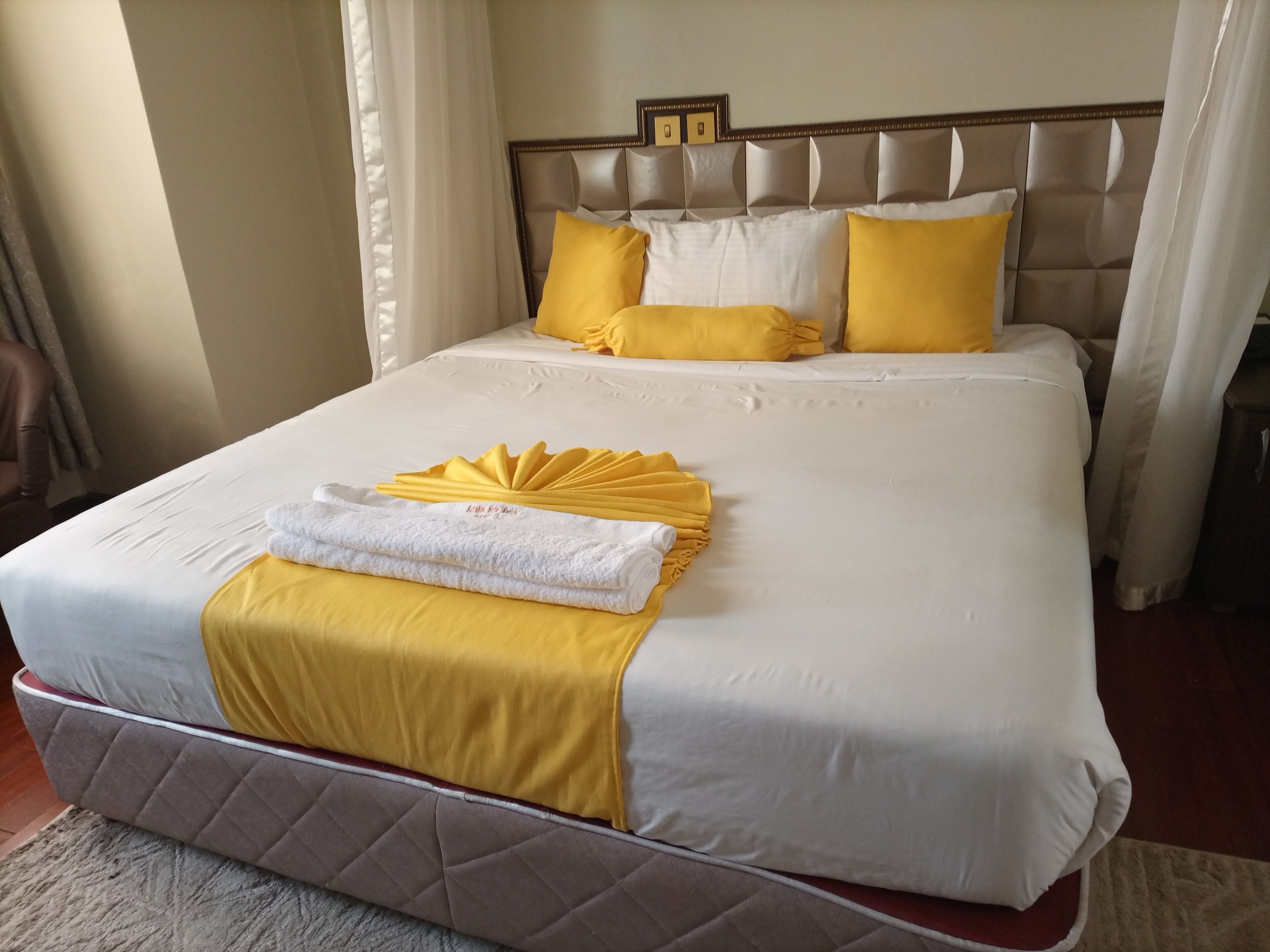 A neatly made bed with a white and yellow bedspread, a quilted headboard, and a decorative towel arrangement.