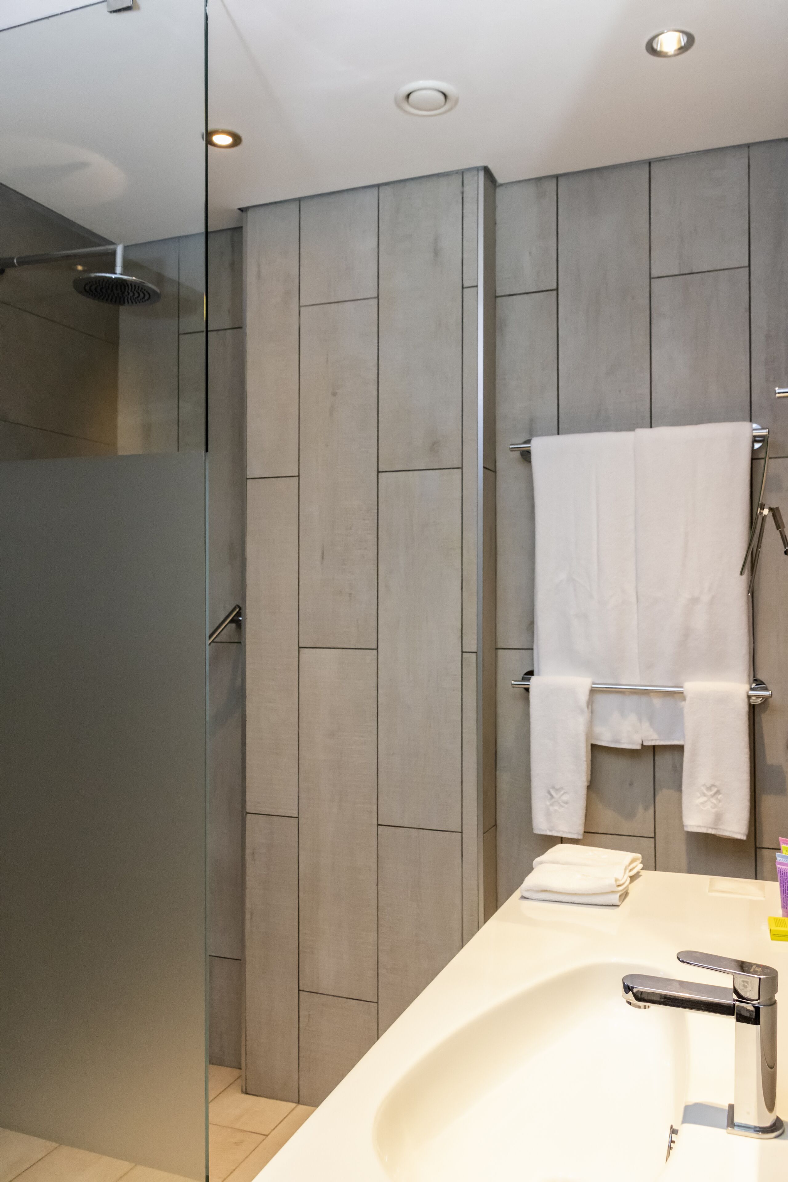 A modern bathroom with a glass shower enclosure, a white sink, and a towel rack.