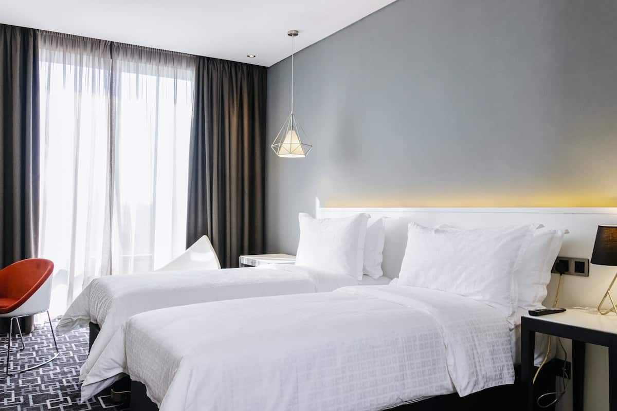 A hotel room with two beds, a chair, a nightstand, and a lamp.