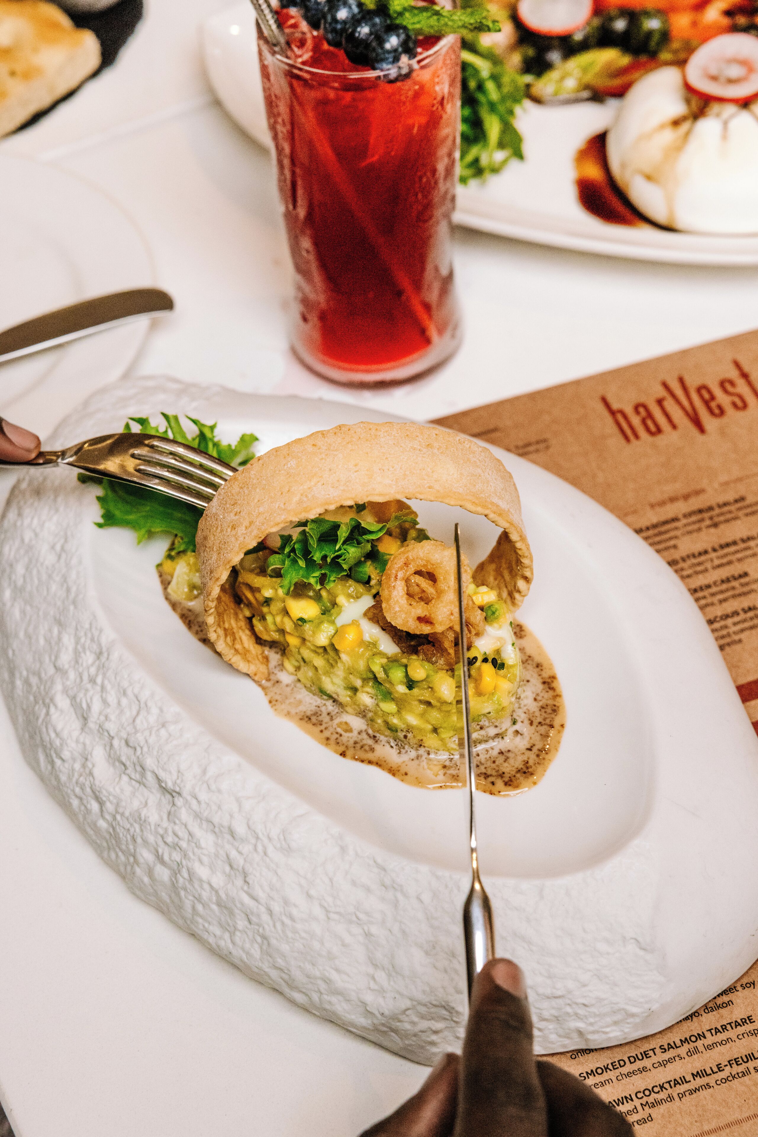 A plate with a sandwich cut in half, a fork, and a knife on a table with a menu.