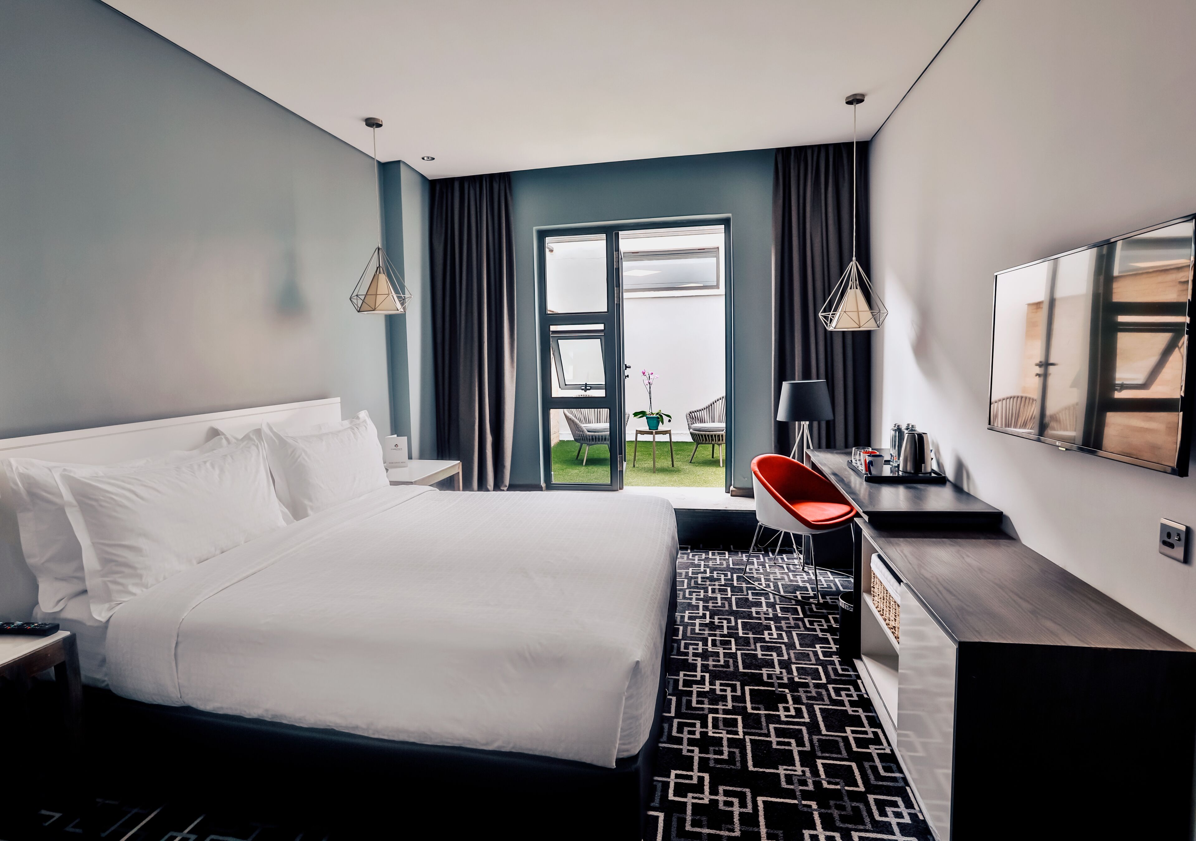 A modern hotel room with a large bed, a desk, a chair, and a view of the outdoors.
