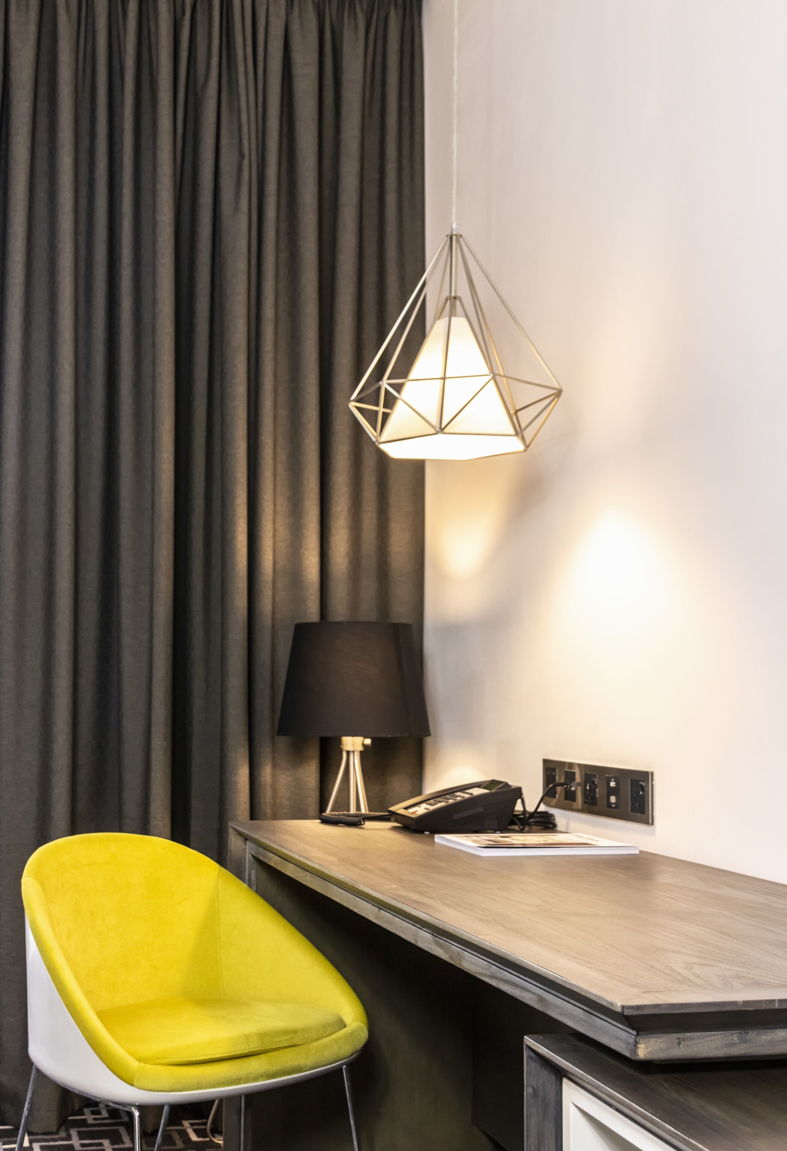 Una camera d'albergo con una scrivania, un telefono, una lampada e una sedia giallo brillante.