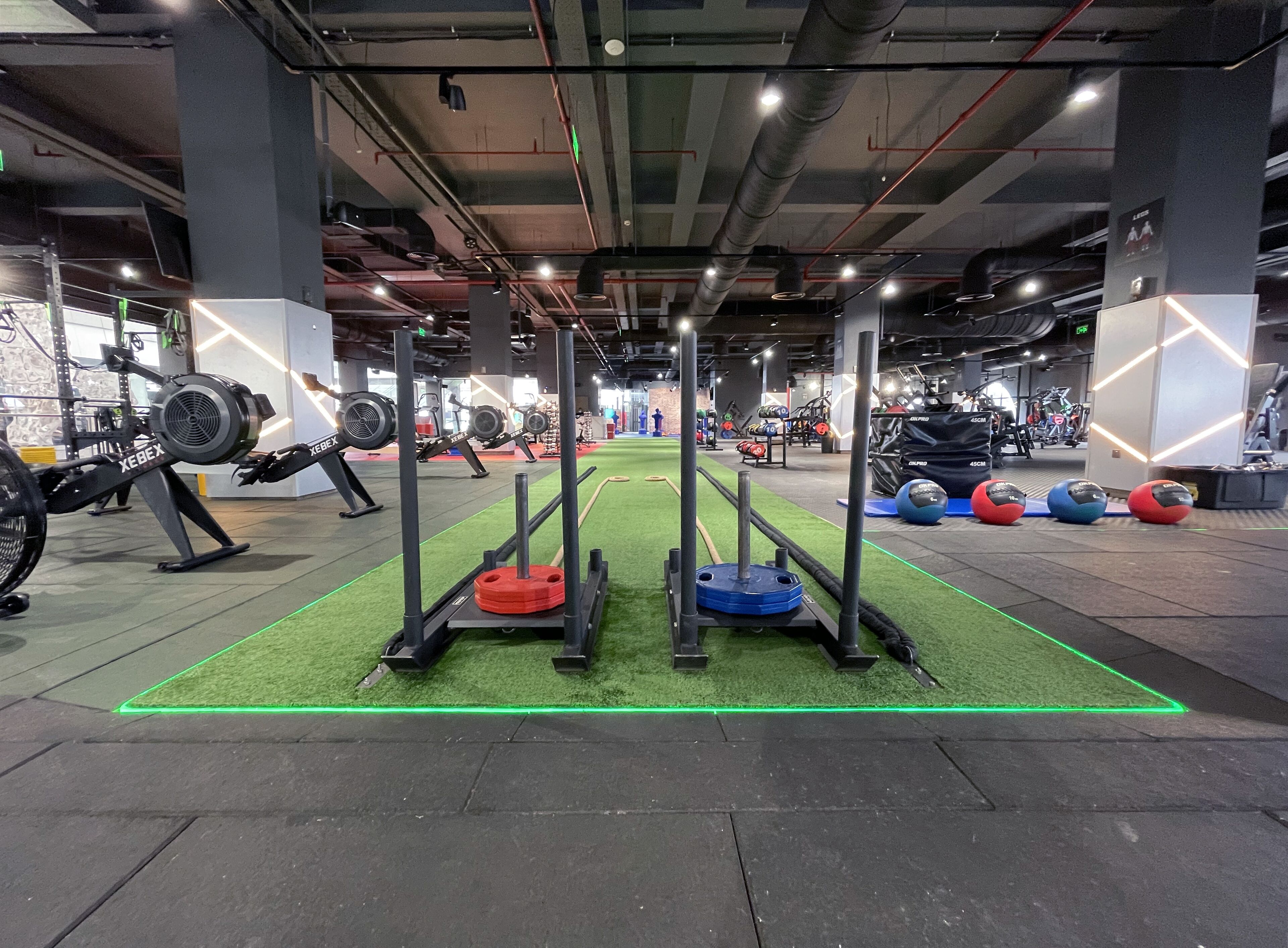 A gym with weightlifting equipment, a green artificial turf area, and various exercise machines.