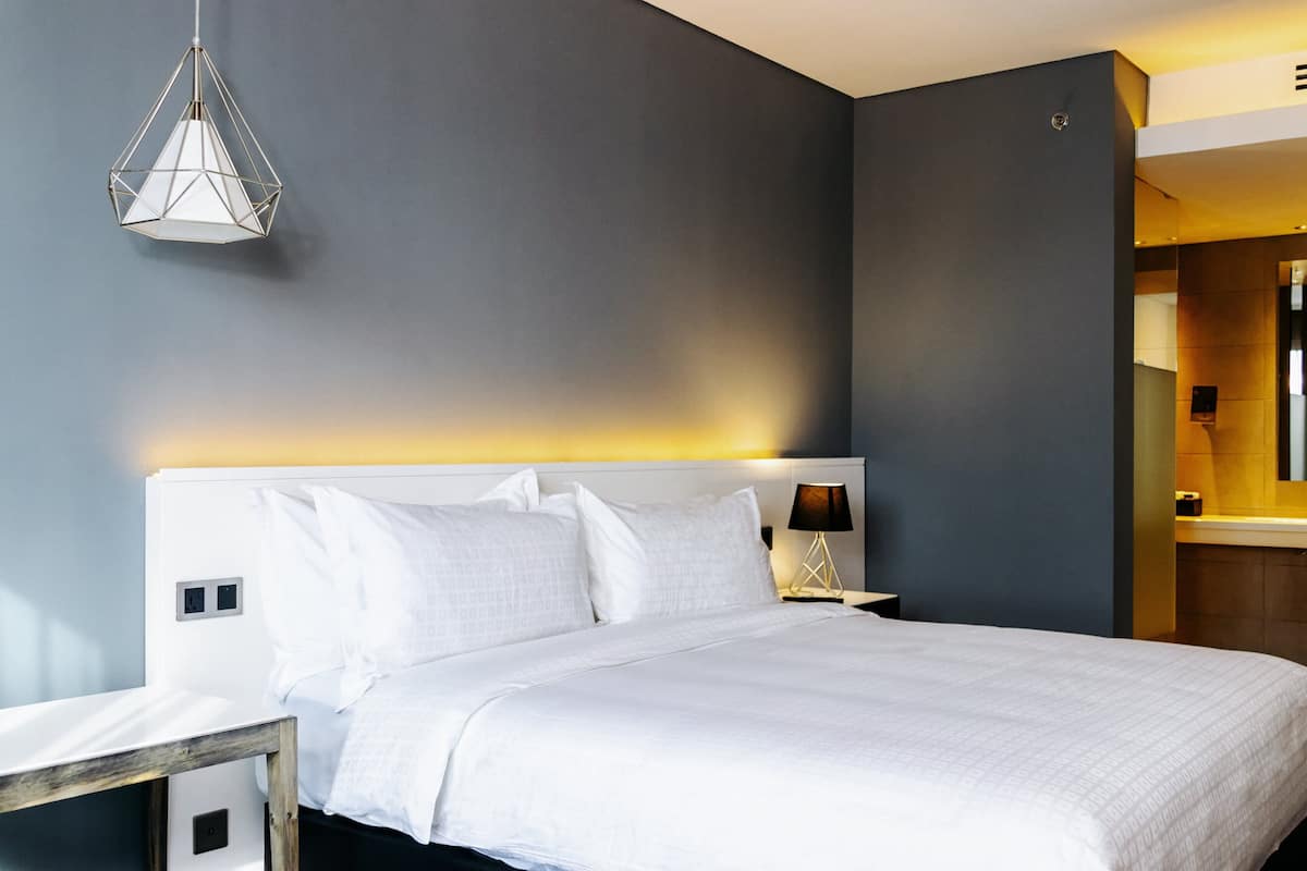 A modern hotel room with a large bed, a bedside table, a lamp, and a geometric pendant light.