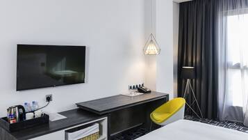 A modern hotel room with a flat-screen TV, a desk with a telephone, a yellow chair, and a large bed.