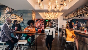 A bar area with multiple stools and tables, a mural on the wall, and a variety of bottles and glasses on shelves. - Trademark Hotel (Nairobi)