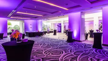 A modern hotel lobby with a purple-lit ceiling, a patterned carpet, and a glass partition wall.