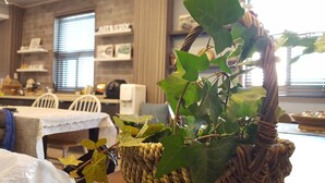 A dining area with a wicker basket containing green leaves, a white table with a tablecloth, and a wall with framed pictures and a sign that reads "ARTSTAY". - Art N Stay - Hostel (Suncheon)