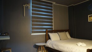 A bedroom with a bed, a small round table, a chair, and a window with blinds. - Art N Stay - Hostel (Suncheon)