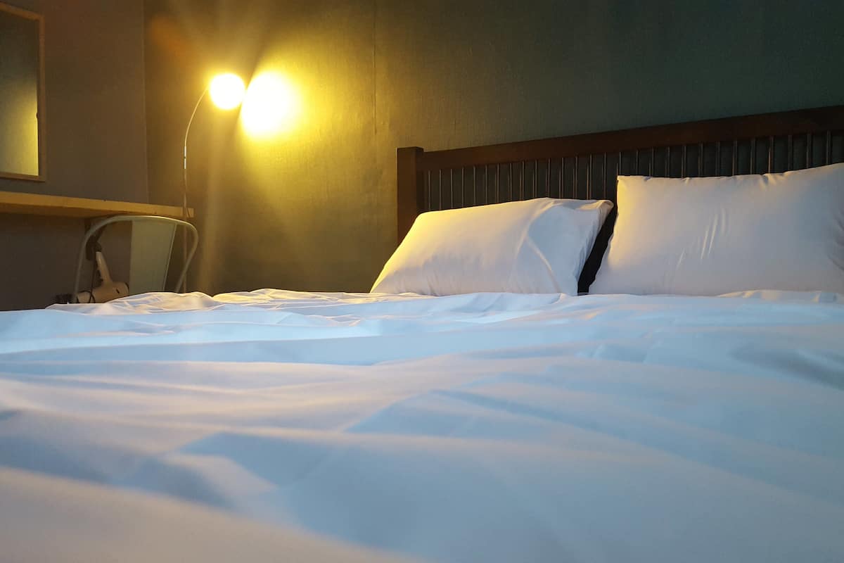 Un lit bien fait, avec du linge de lit blanc, dans une chambre d’hôtel.