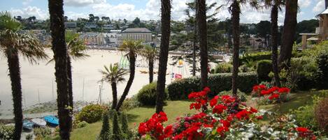 Vista costera con palmeras, una playa y un edificio al fondo.