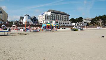 Una playa con un edificio grande al fondo, un parque infantil con juegos de colores y una zona de arena.