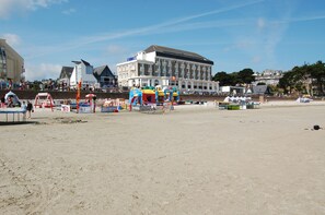 Une plage avec un grand bâtiment en arrière-plan, une aire de jeux dotée d’équipements colorés et une zone de plage sablonneuse.