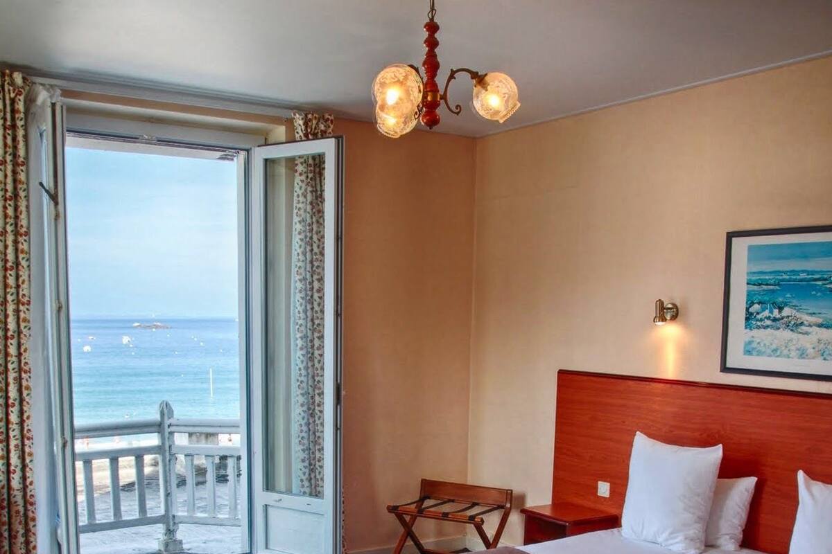 Une chambre d’hôtel comprenant un lit, un bureau, une chaise, un balcon avec vue sur la mer et un lustre.