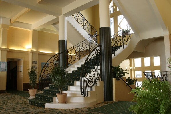 A grand staircase with ornate black railings, flanked by large potted plants and white steps. - Grand Hôtel de Trestraou (Perros-Guirec)