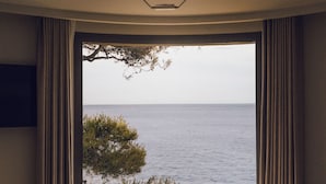 Un dormitorio con una ventana grande con vistas al mar, una cama y cortinas.