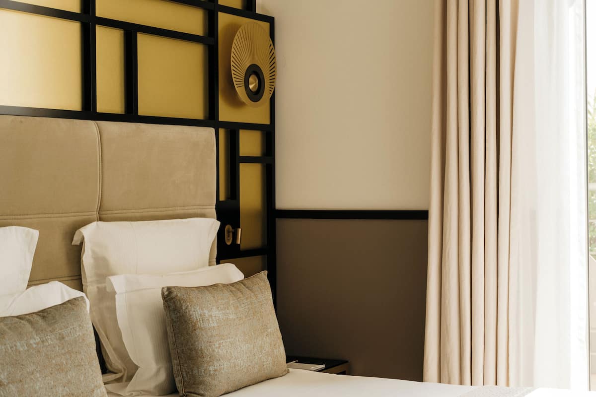 A hotel room with a large bed, a headboard with a geometric design, and a window with curtains.