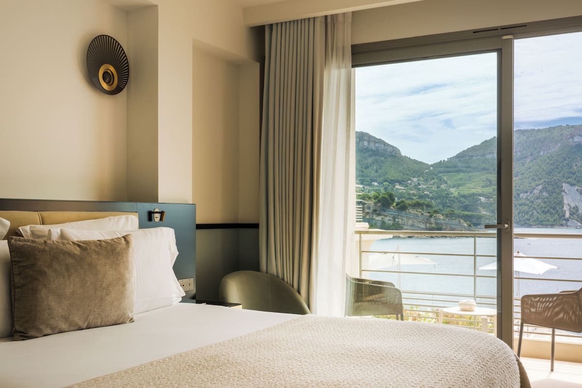 A hotel room with a large bed, a view of a mountainous landscape, and a balcony with outdoor seating.