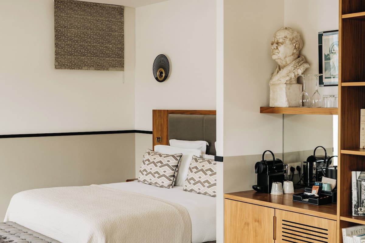 A modern hotel room with a bed, bedside table, and a small kitchenette area.