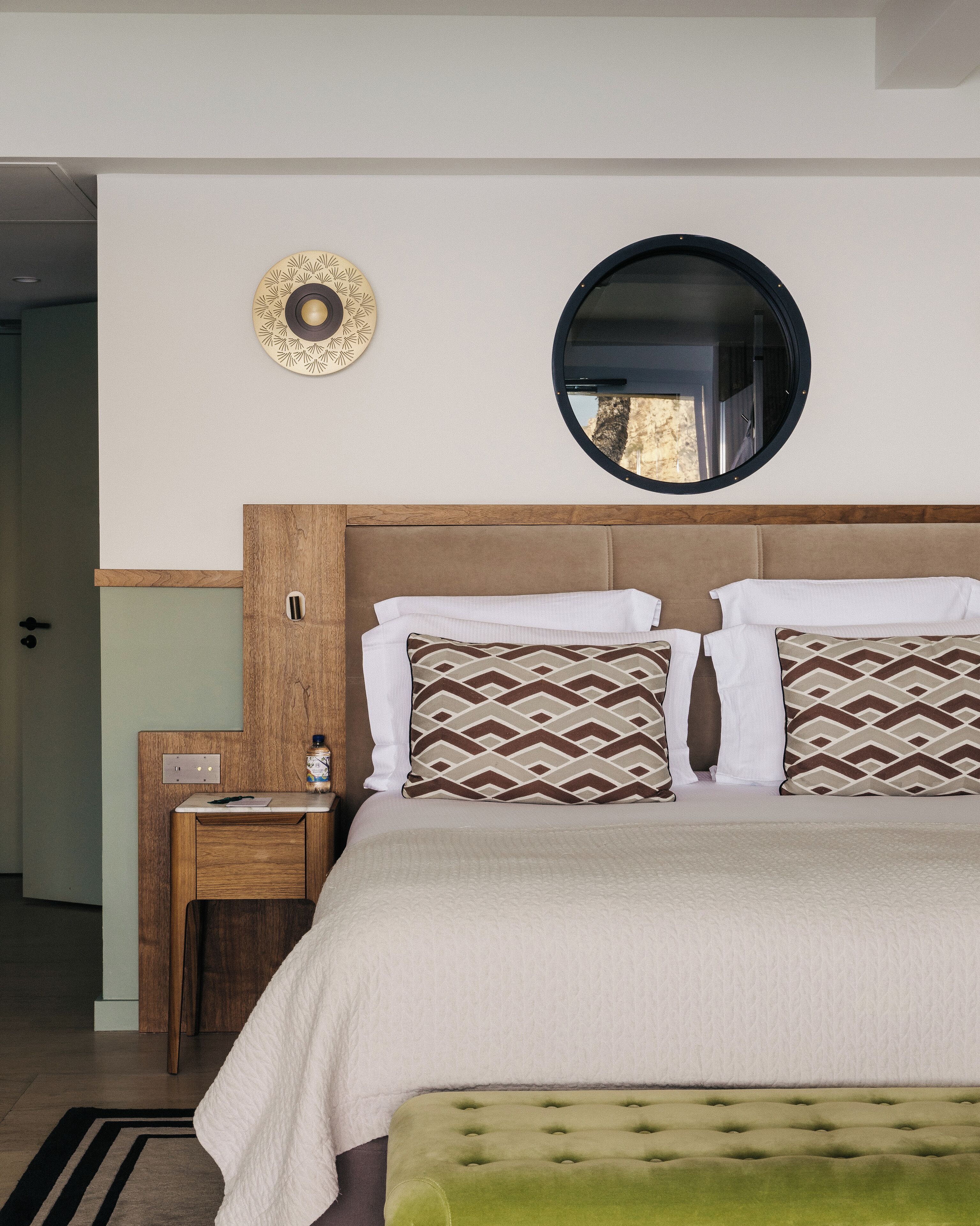 A neatly arranged hotel room with a bed, bedside tables, a mirror, and a wall-mounted decorative item.