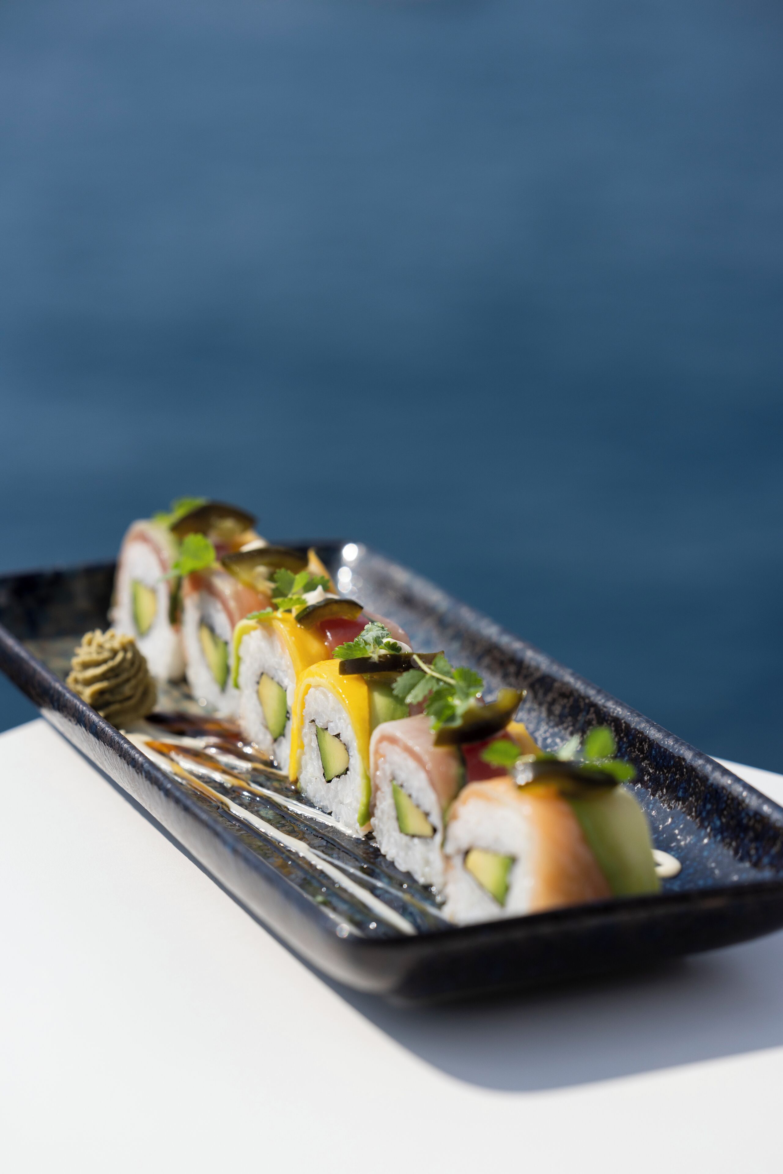 A sushi platter with various types of sushi on a rectangular black plate.