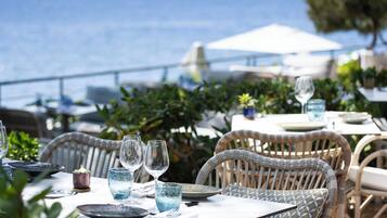 Un área de comedor al aire libre con sillas y mesas de mimbre, con vista al mar.