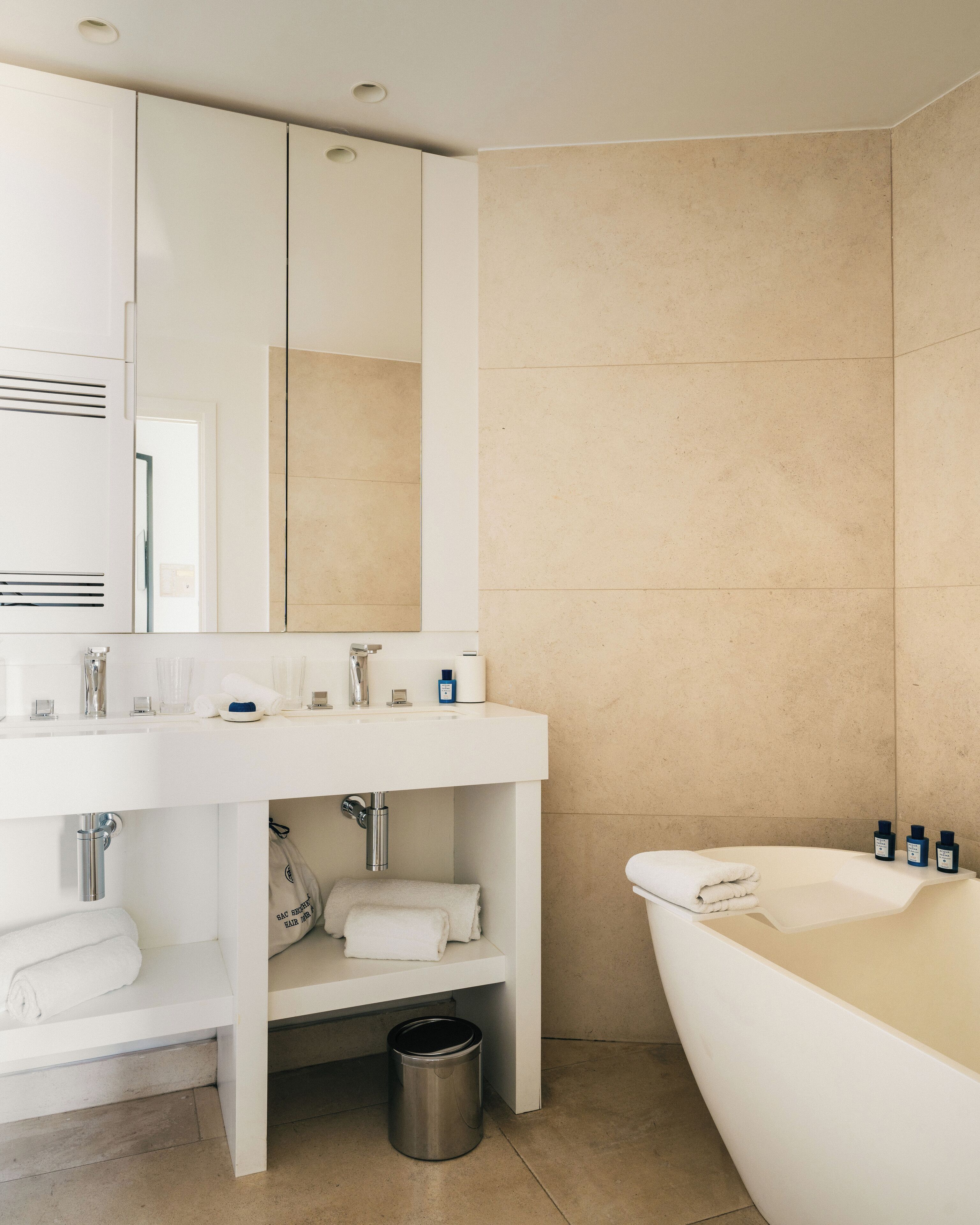 Un baño moderno con tocador blanco, un espejo grande, una bañera y paredes cubiertas de baldosas color beige.