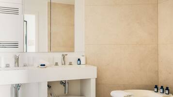 Un baño moderno con tocador blanco, un espejo grande, una bañera y paredes cubiertas de baldosas color beige.