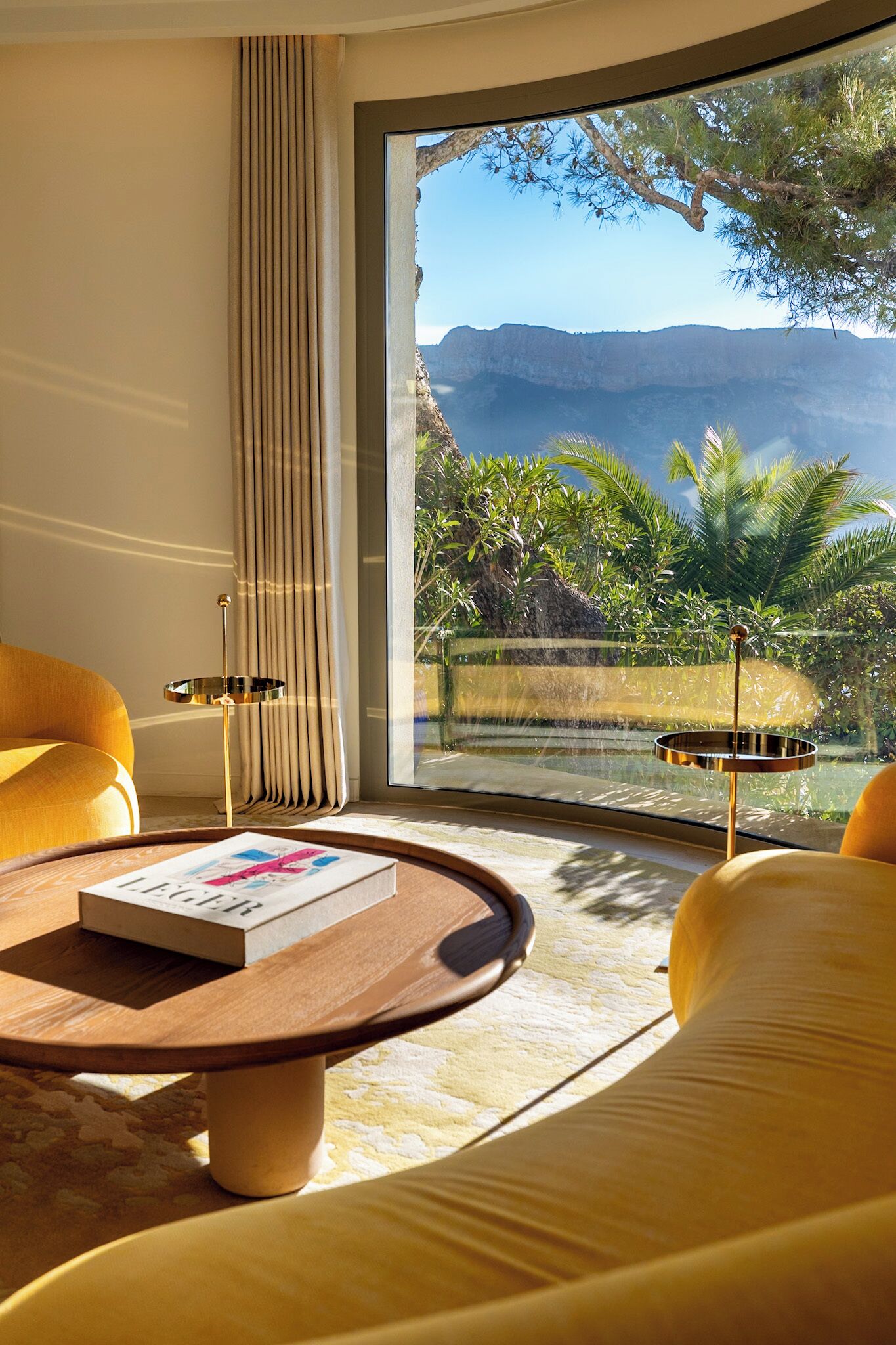 A modern living room with a large window, a round coffee table, and yellow sofas.