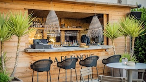 A wooden bar area with hanging lights, bar stools, and a table with chairs. - Hôtel Les Roches Blanches (Cassis)