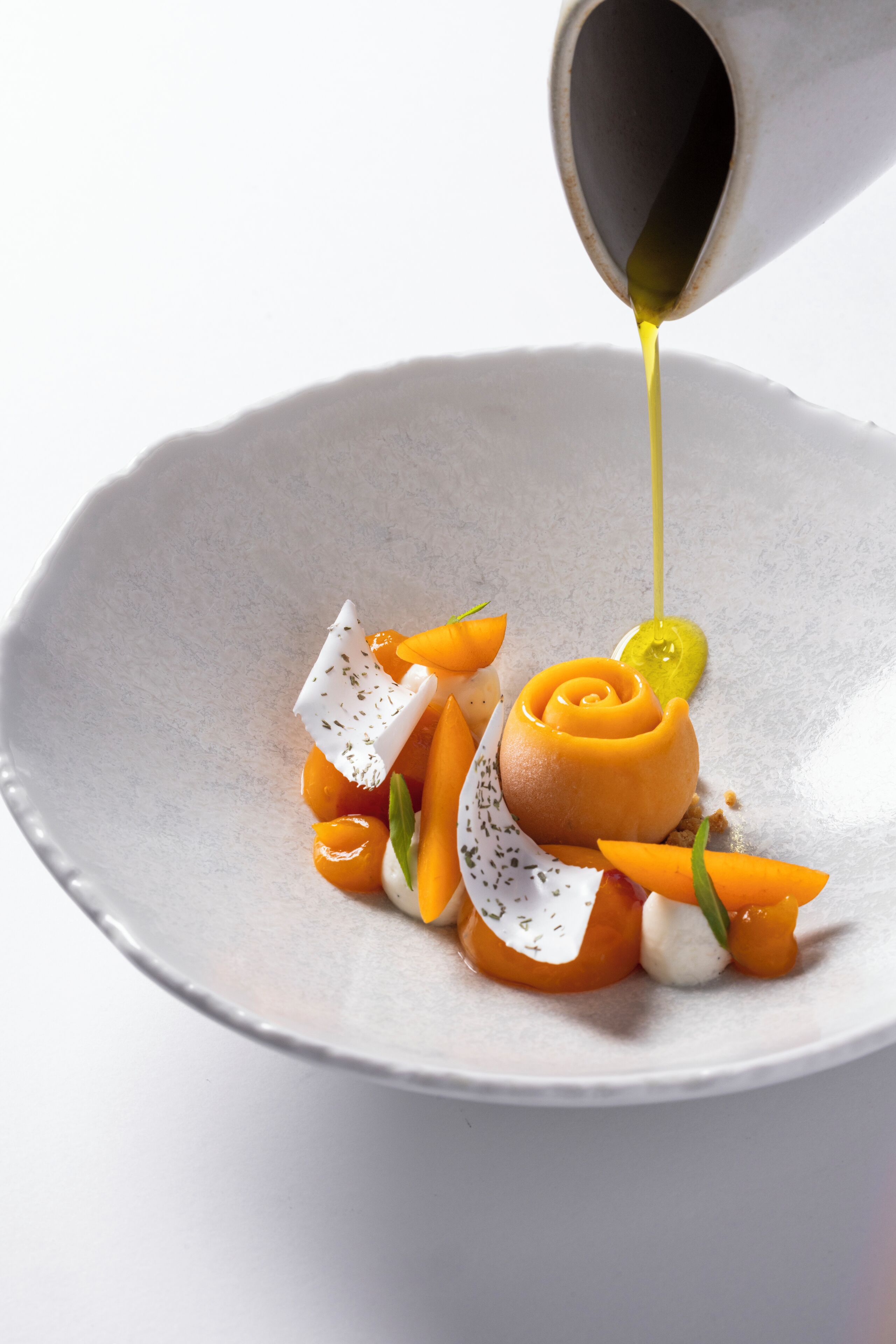 A white ceramic plate with a dessert consisting of a caramelized fruit centerpiece, garnished with herbs and a dollop of cream.