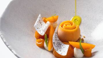 A white ceramic plate with a dessert consisting of a caramelized fruit centerpiece, garnished with herbs and a dollop of cream.