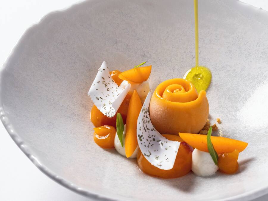 A white ceramic plate with a dessert consisting of a caramelized fruit centerpiece, garnished with herbs and a dollop of cream.