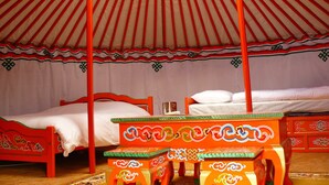 A traditional yurt with a four-poster bed and a wooden table with intricate designs. - Du coq à l'âne (Saint-Georges-de-Rex)