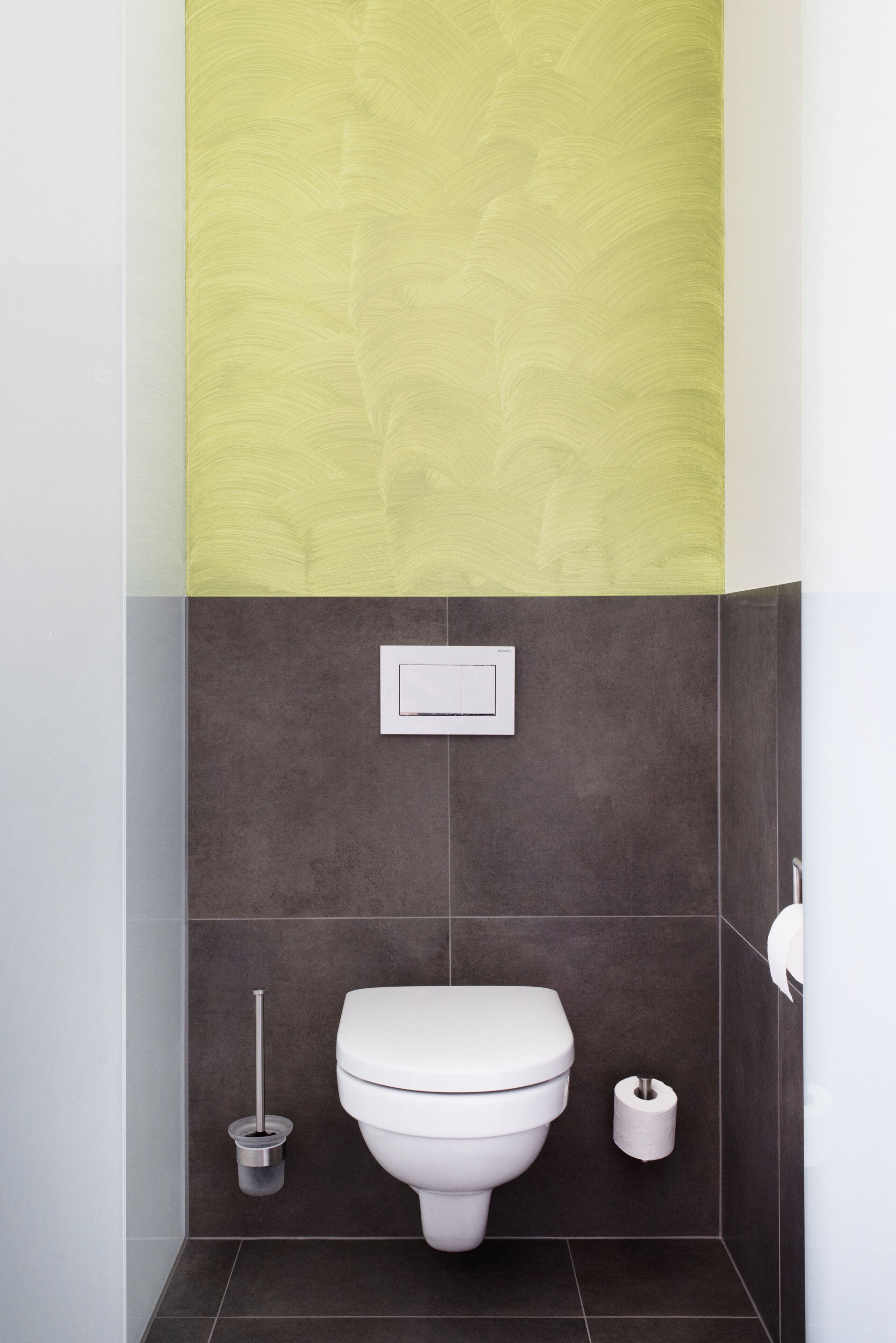 Een moderne badkamer met een wit toilet, een toiletrolhouder en een bedieningsknop op de muur.