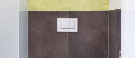 Een moderne badkamer met een wit toilet, een toiletrolhouder en een bedieningsknop op de muur.